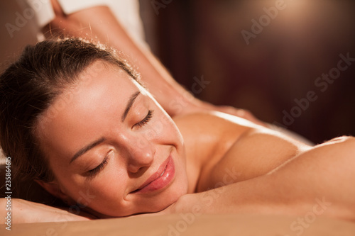 Close up of a gorgeous happy young woman smiling with her eyes closed, enjoying soothing massage at spa center. Beautiful female relaxing at pamper salon, copy space. Service, travel, tourism concept