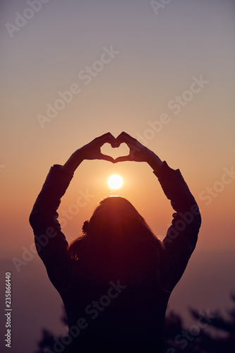 Girl making heart - shape sign with hands at sunset / sunrise time.