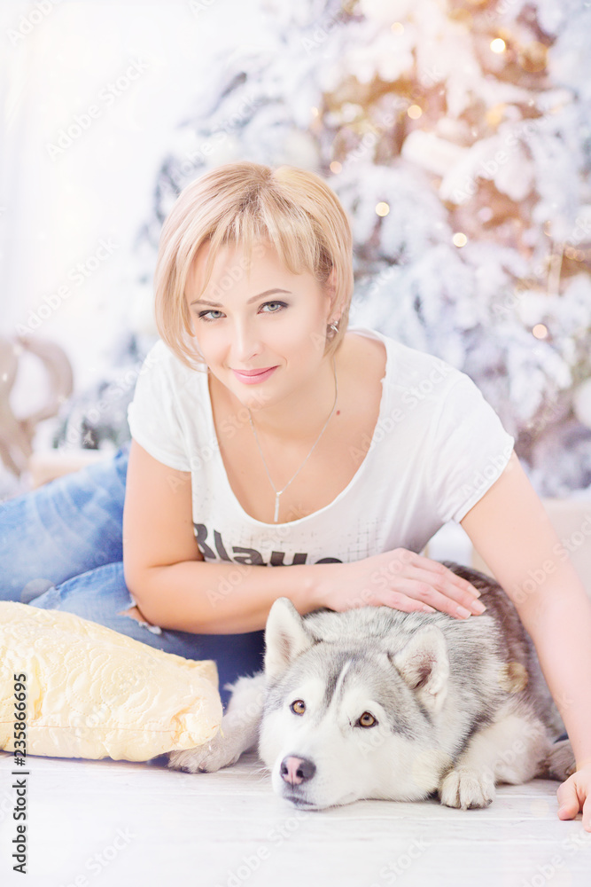 Beautiful blonde woman sits with husky dog near christmas tree. Beautiful blonde woman sits with husky dog near christmas tree.