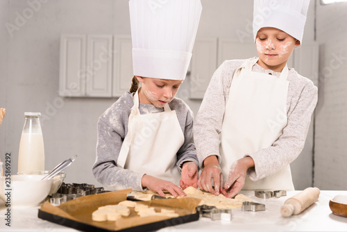 kids in chef hats and aprons cutting out dough for cookies at table in kitchen