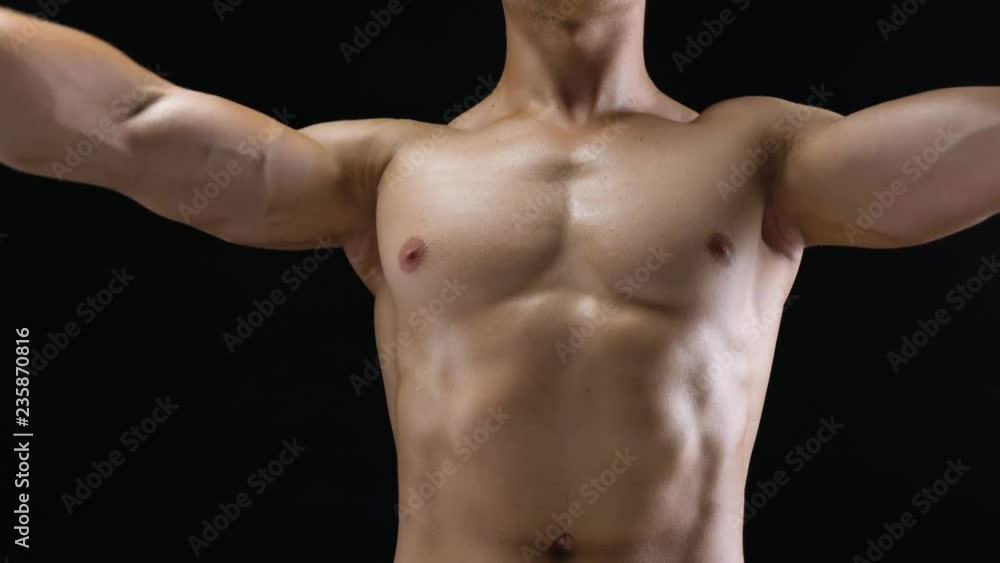 Athletic man doing exercise on his shoulders with elastic band on a black background in studio Athletic man doing exercise on his shoulders with elastic band on a black background in studio