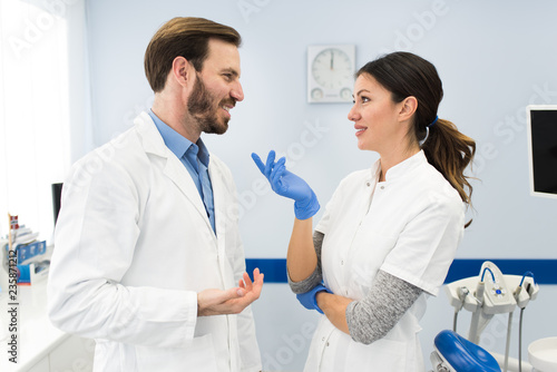 Young modern dentists smiling. Female dentist and male dentist talking and smiling working together in dentist office. Happy dentists concept.
