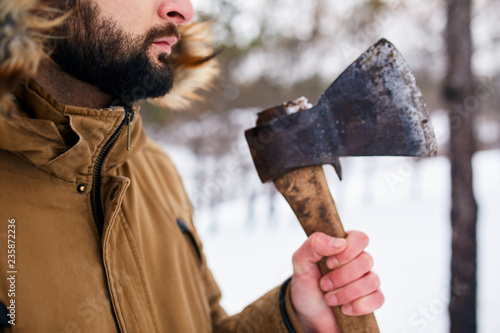 Beard and axe. Lumberjack standing with weathered rusty axe in his hand. Close view, unrecognizable man in forest. Neatly trimmed beard line. Trimmer or barber commercial.