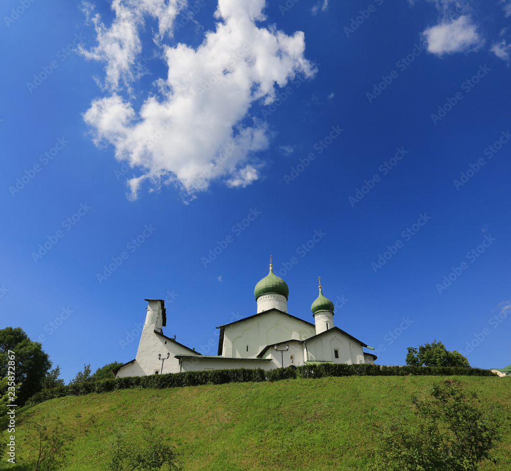 White-stone church against the blue sky, white clouds and green grass