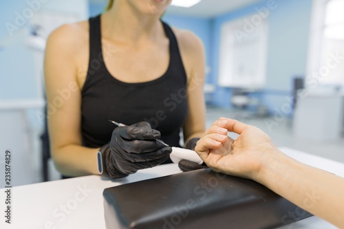 Closeup process of professional manicure. Manicurist woman hands in black gloves making manicure using professional tools. Nail and hand care in beauty salon