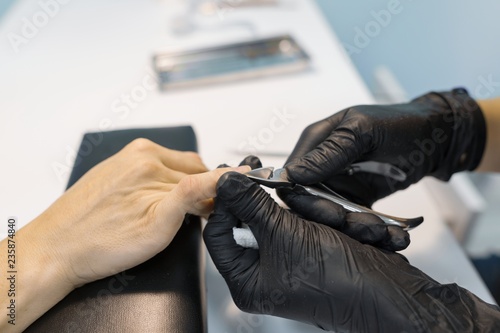 Closeup process of professional manicure. Manicurist woman hands in black gloves making manicure using professional tools. Nail and hand care in beauty salon