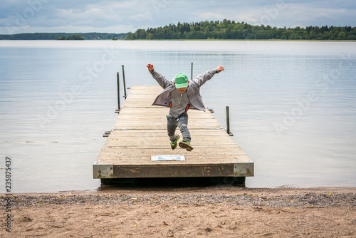 Front view of a young boy running on a jetty and jumps in air towards a beach.