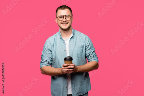 handsome happy man holding coffee to go and smiling at camera isolated on pink © LIGHTFIELD STUDIOS