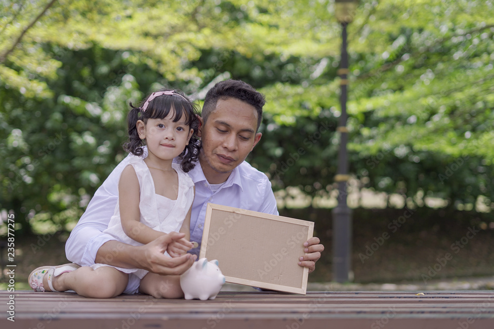A man with his daughter with piggy bank and blank board for copy space. Financial and future planning concept. A man with his daughter with piggy bank and blank board for copy space. Financial and future planning concept.