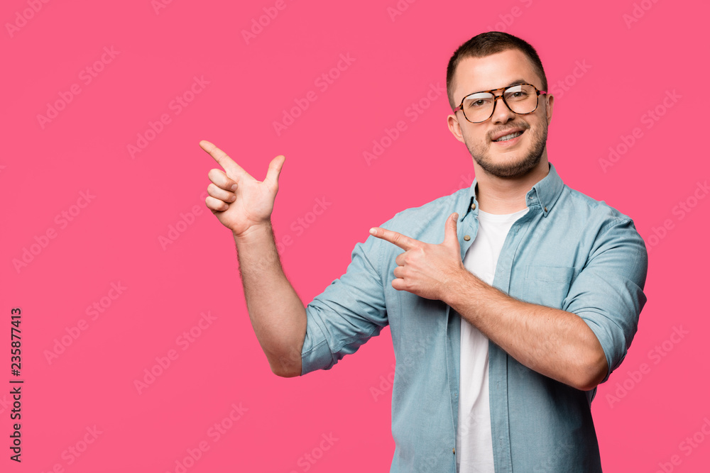 happy young man pointing with fingers at copy space and smiling at camera isolated on pink happy young man pointing with fingers at copy space and smiling at camera isolated on pink