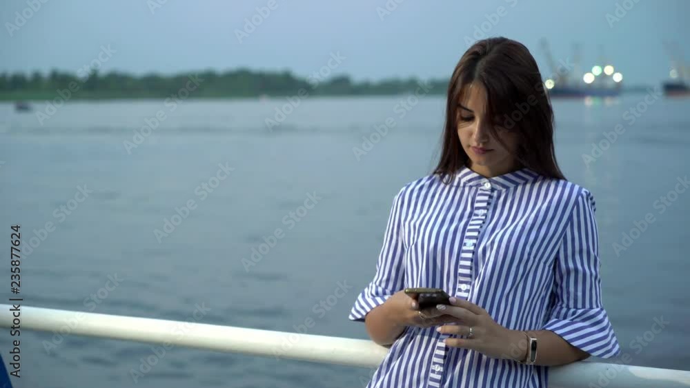 Glamour young woman surfing the net and seeking photos on a river quay in summer Glamour young woman surfing the net and seeking photos on a river quay in summer