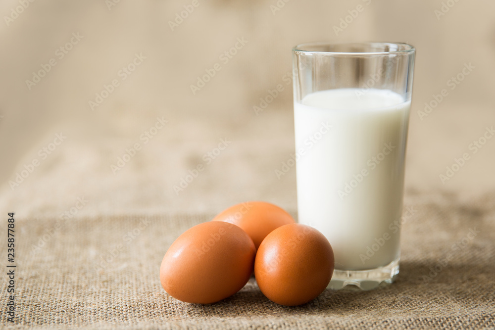Milk in glass and chicken eggs on light brown textile background. Healthy eating Milk in glass and chicken eggs on light brown textile background. Healthy eating