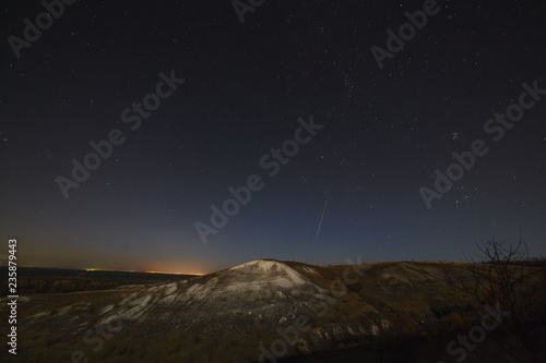 Night sky with stars and a meteorite over the hills. The landscape was photographed on a long exposure.