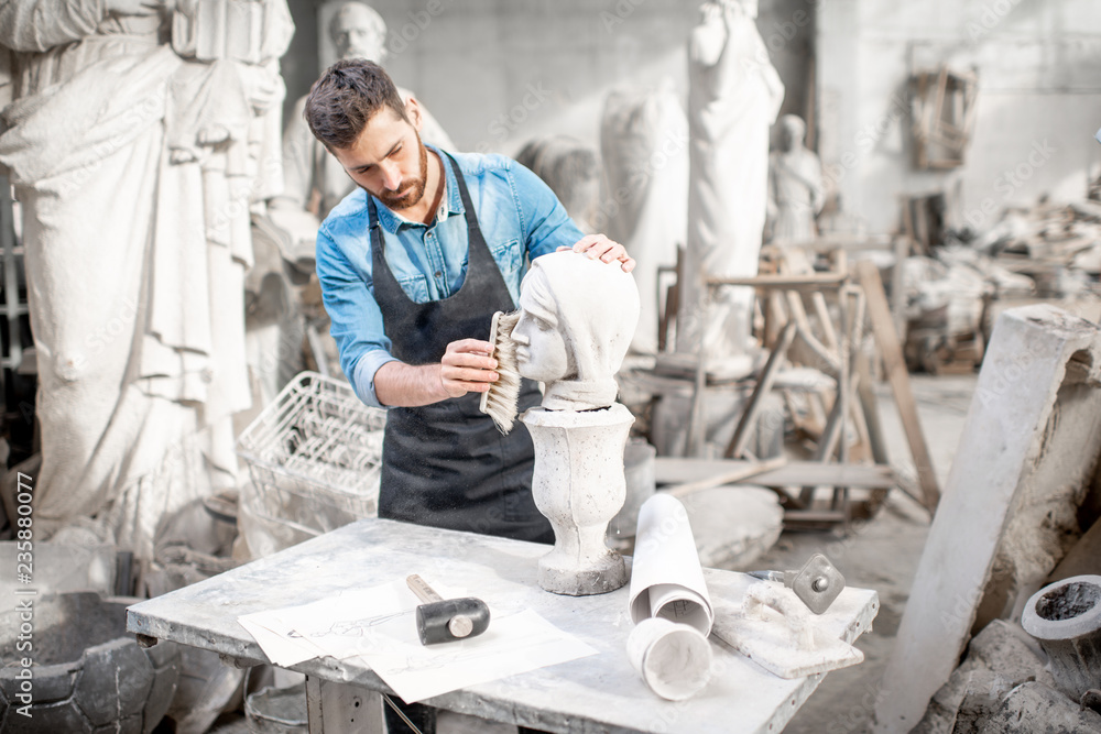 Handsome sculptor brushing stone head sculpture on the table in the atmospheric studio Handsome sculptor brushing stone head sculpture on the table in the atmospheric studio