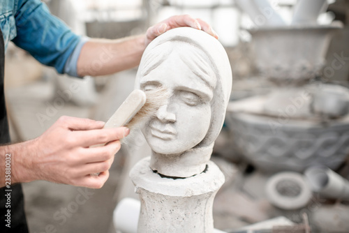 Sculptor working with sculpture of the female head cleaning with brush in the old studio. Close-up view with no face