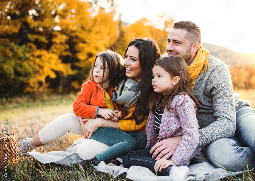 A portrait of young family with two small children in autumn nature at sunset.