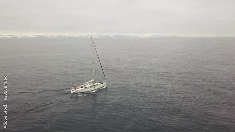 Sailing yacht floating in sea and snowy islands and highlands on skyline drone view Sailing yacht floating in sea and snowy islands and highlands on skyline drone view