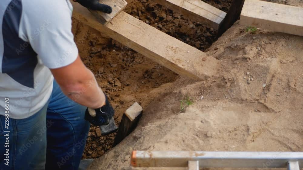 Builder Scores Hammer A Wooden Board In The Ground In The Pit For Foundation Builder Scores Hammer A Wooden Board In The Ground In The Pit For Foundation
