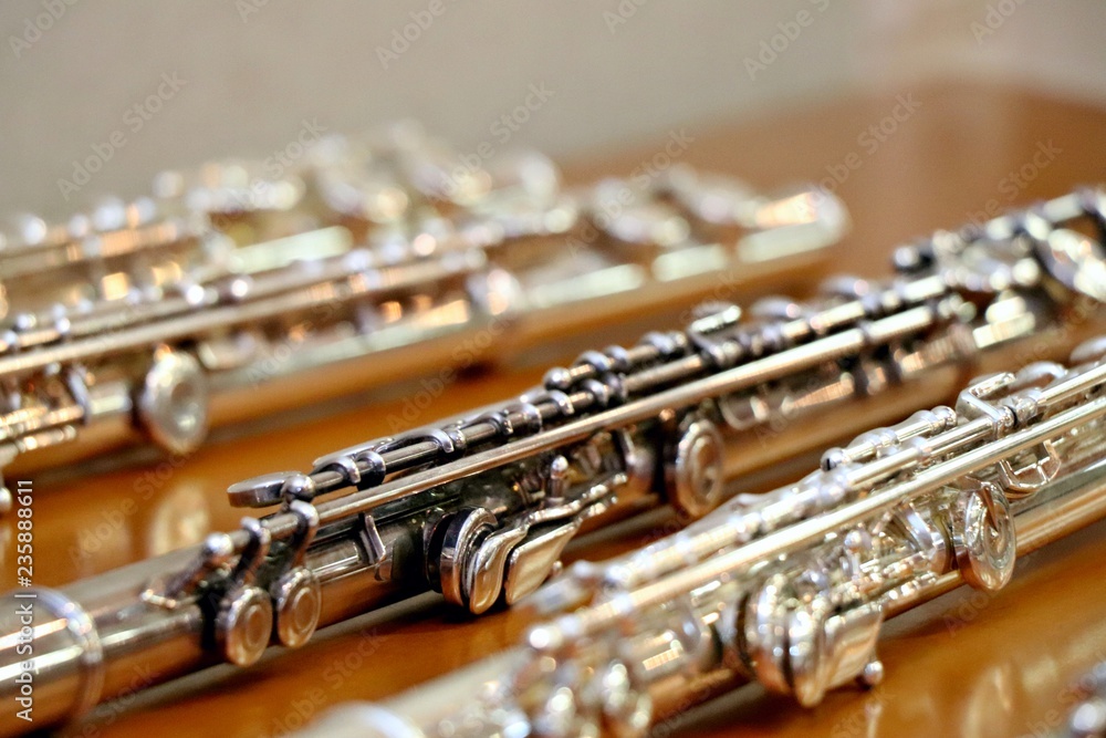 Fototapeta premium Blurry soft focused set of silver flutes on the wooden table close up. Musik background. Selected focus.