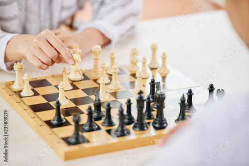 Faceless people playing chess and moving figures on wooden board at table photo