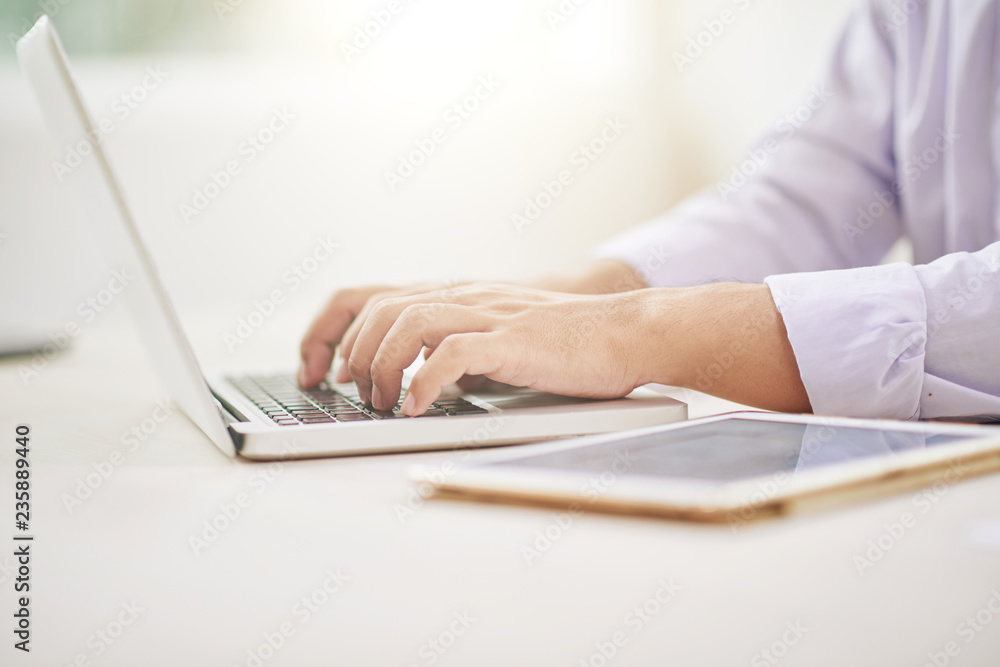 Faceless side view of man in shirt typing on laptop sitting at desk in office Faceless side view of man in shirt typing on laptop sitting at desk in office