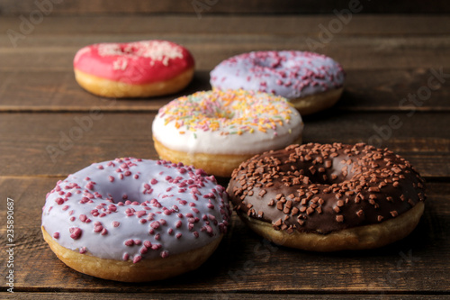 Assorted sweet donuts with icing and sprinkles on a brown wooden table.