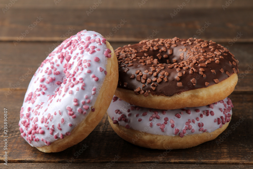 Different sweet donuts with icing and sprinkling close-up stacked on a brown wooden table.