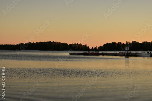 Golden sunset by the lake with boats and an island full of trees