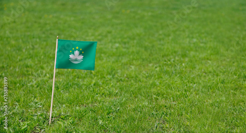 Macau flag. Photo of Macau flag on a green grass lawn background. Close up of national flag waving outdoors.