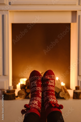 cropped view of woman in woolen winter socks with fireplace on background
