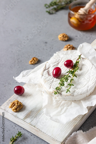 Baked camembert with cranberry, walnuts, honey and thyme on parchment paper. Brie type of cheese. Grey slate, stone or concrete table. Copy space.