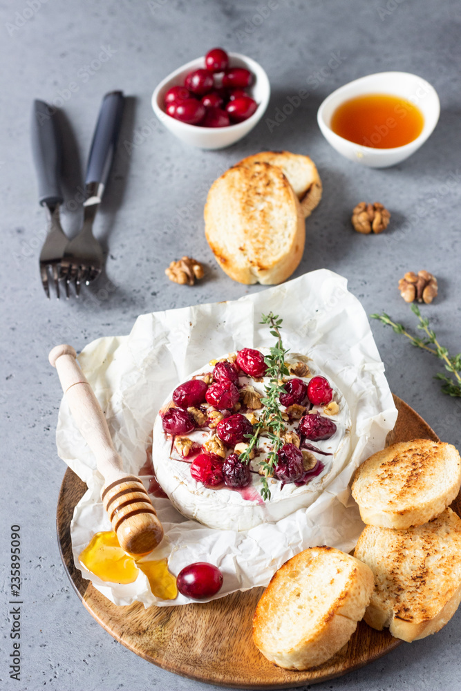 Baked camembert with cranberry, walnuts, honey and thyme on parchment paper. Brie type of cheese. Grey slate, stone or concrete table. Copy space. Baked camembert with cranberry, walnuts, honey and thyme on parchment paper. Brie type of cheese. Grey slate, stone or concrete table. Copy space.