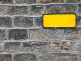 a blank yellow metal sign with empty space for copy on an old stone wall background