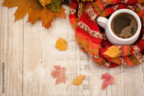  A cup of coffee wrapped in a scarf on a table covered with colorful leaves. © seredan