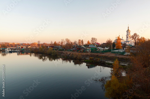 panoramic view of the church which is situated on the bank of the river among private houses against the background of blue sky reflected in water