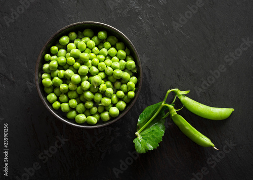 A bowl of fresh green peas with two pea pods. photo