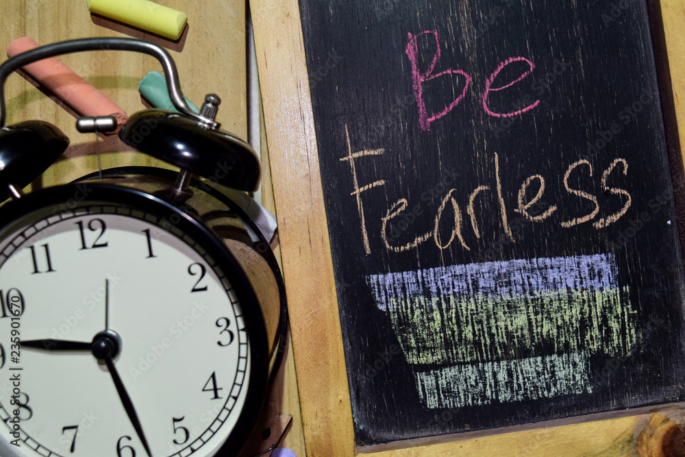 Be Fearless on phrase colorful handwritten on chalkboard and alarm clock with motivation, inspiration and education concepts. Table background Be Fearless on phrase colorful handwritten on chalkboard and alarm clock with motivation, inspiration and education concepts. Table background