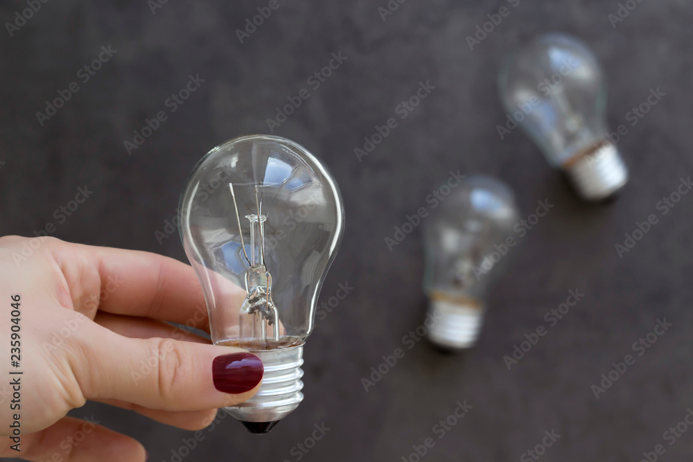 Hand holding lamp bulb and two another on the grey concrete background. Soft focus, close-up, copy space Hand holding lamp bulb and two another on the grey concrete background. Soft focus, close-up, copy space