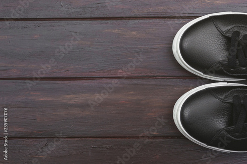 Casual black leather sneakers on wooden background