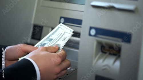 Man counting dollars withdrawn from ATM, 24h service, easy banking operation