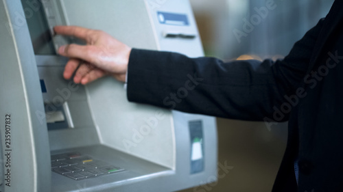 Client entering pin code on ATM to receive money, banking services, withdrawing