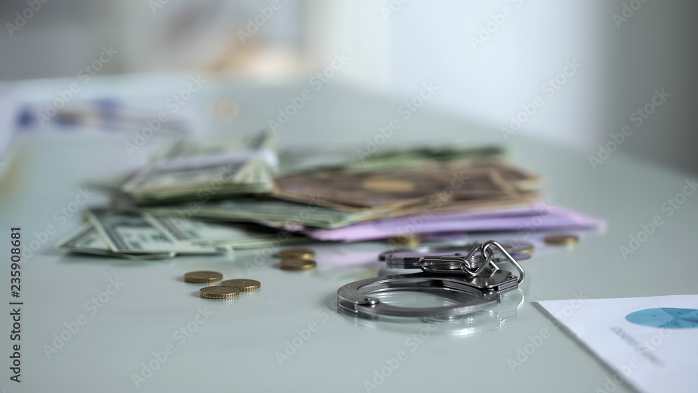 Handcuffs and money on table, bribery punishment, financial control system Handcuffs and money on table, bribery punishment, financial control system
