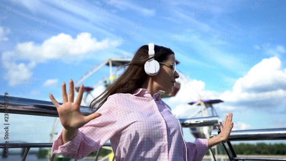 Obraz premium Positive brunette woman in headphones dancing on pier, having fun on vacation