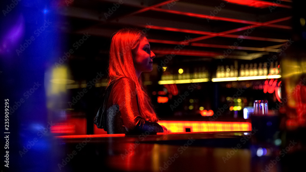 Confident beautiful young girl sitting in night club near bar, evening party