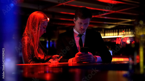 Gadget addicted couple using their smart phone in bar  lack of communication
