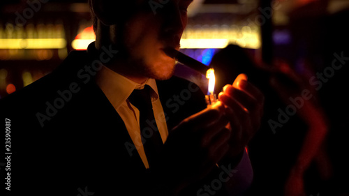 Cuadro en lienzo Businessman lighting cigar in elite bar, night atmosphere, dance floor, relax