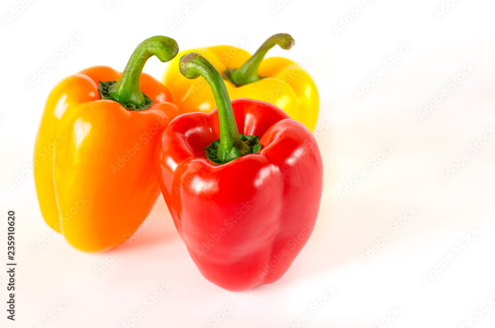 Juicy red, orange and yellow peppers with a green tail lies on a white background Juicy red, orange and yellow peppers with a green tail lies on a white background
