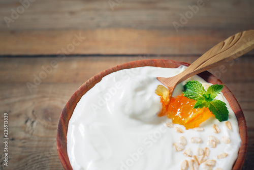 Greek yogurt with oat flakes and orange jam in a wooden bowl on a rustic wooden table.