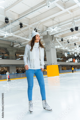 cheerful young woman in white sweater skating on rink alone