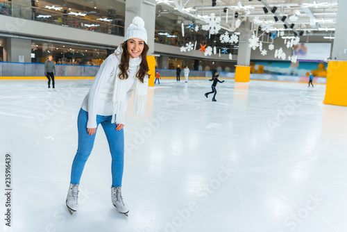 smiling young attractive woman in knitted sweater skating on ice rink alone